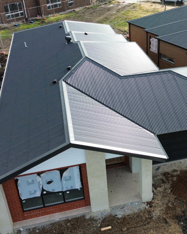 Aerial view of a modern residential home with a dark metal roof and landscaped yard, installed by Pitch Perfect Roof Plumbing.