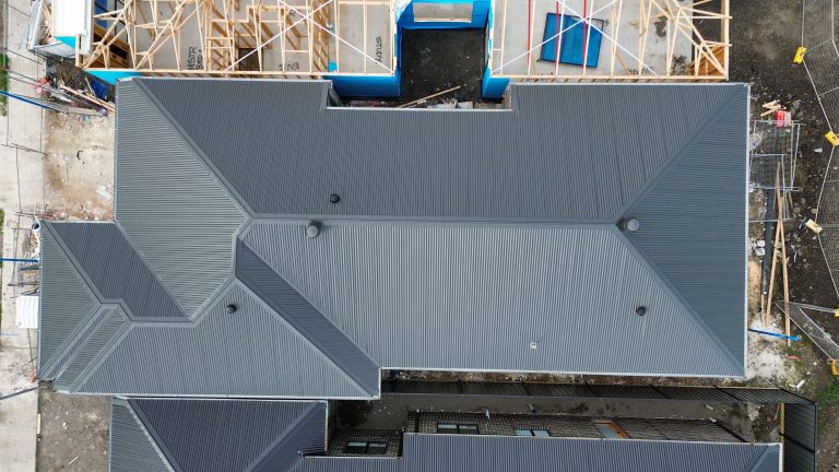 Aerial view of a newly installed dark metal roof on a residential construction project featured on the Pitch Perfect Roof Plumbing Suppliers & Partners page.