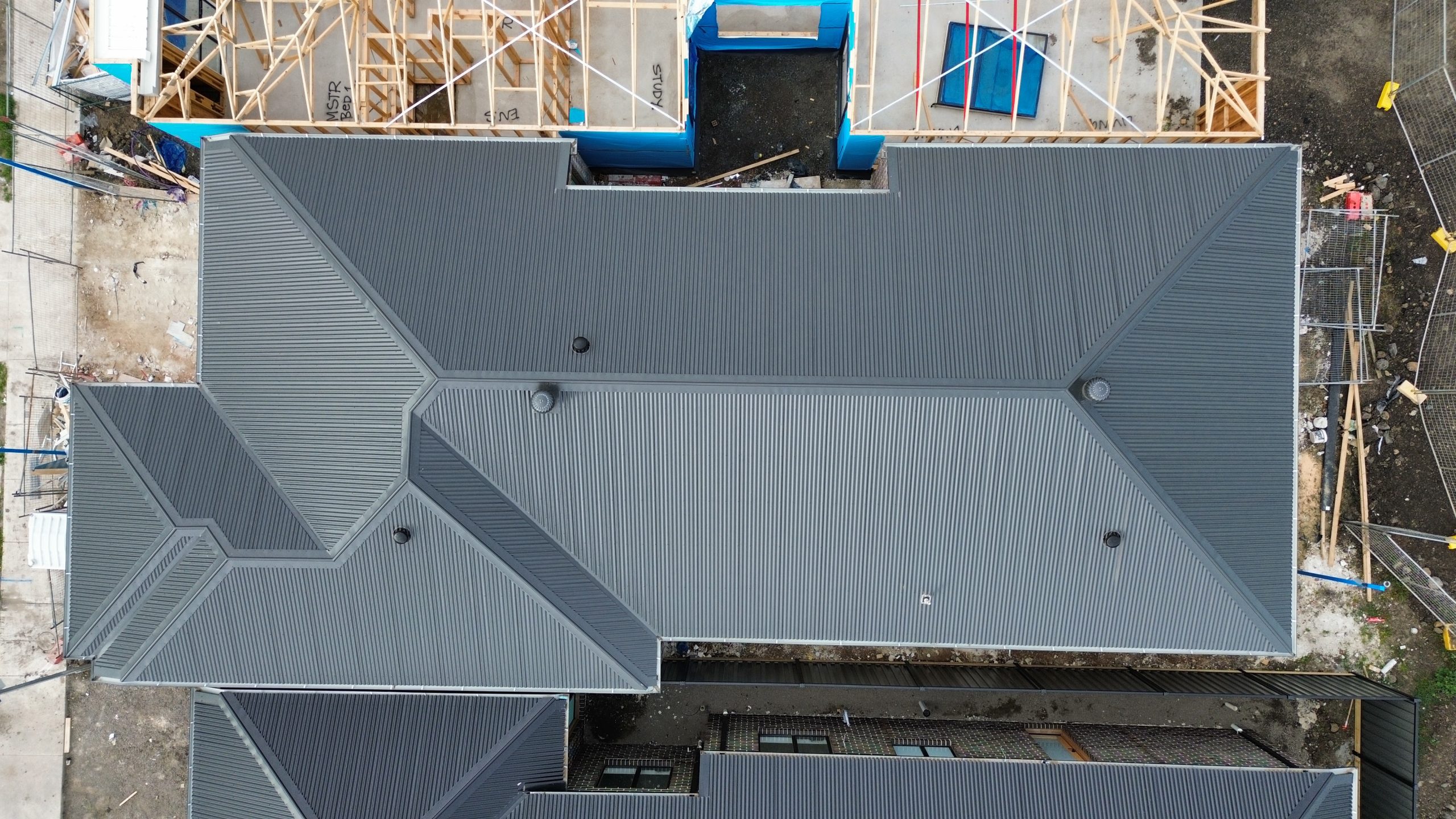 Aerial view of a newly installed dark metal roof on a residential construction project featured on the Pitch Perfect Roof Plumbing Suppliers & Partners page.