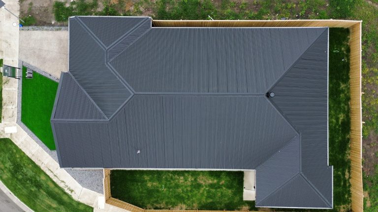 Overhead view of a large residential property showcasing a complex dark metal roof installed by Pitch Perfect Roof Plumbing.