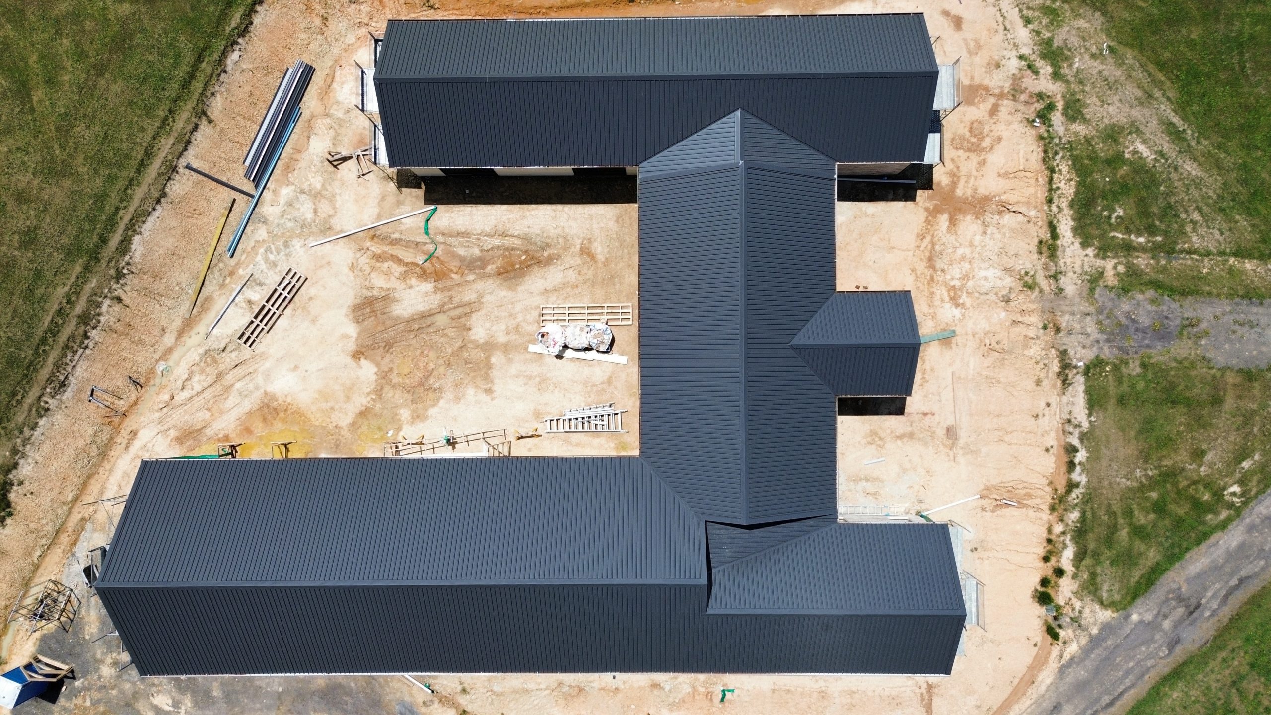 Aerial view of a large residential property mid-construction with newly installed dark metal roofing by Pitch Perfect Roof Plumbing.