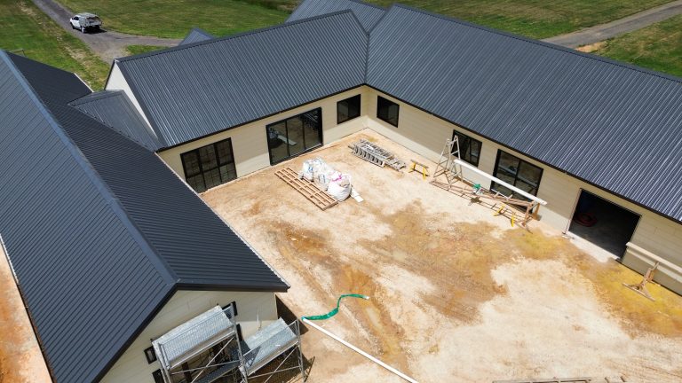 Aerial view of a large U-shaped residential home under construction with new dark metal roofing by Pitch Perfect Roof Plumbing.